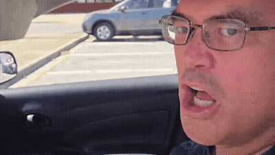 A Man Wearing Glasses Is Sitting In A Car With His Mouth Open GIF