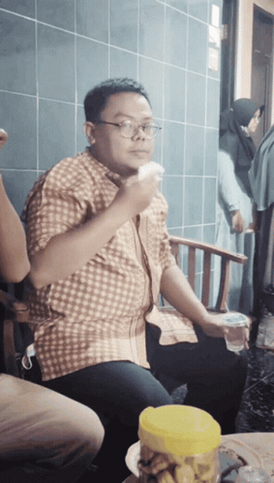 A Man Wearing Glasses Is Sitting In A Chair Eating A Piece Of Food GIF