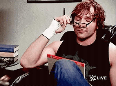 A Man Wearing Glasses Is Sitting In A Chair With A Wwe Live Logo On His Shirt GIF