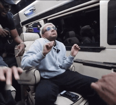 A Man Wearing Glasses Is Sitting In A Chair With His Hands Up In The Air GIF