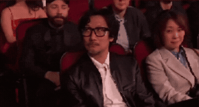 A Man Wearing Glasses Is Sitting In A Theatre Watching A Movie . GIF