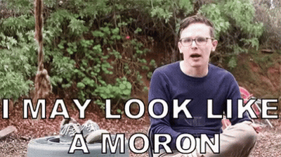 A Man Wearing Glasses Is Sitting In The Dirt With The Words I May Look Like A Moron Below Him GIF