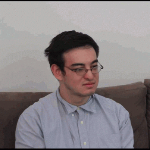 A Man Wearing Glasses Is Sitting On A Couch And Making A Funny Face GIF