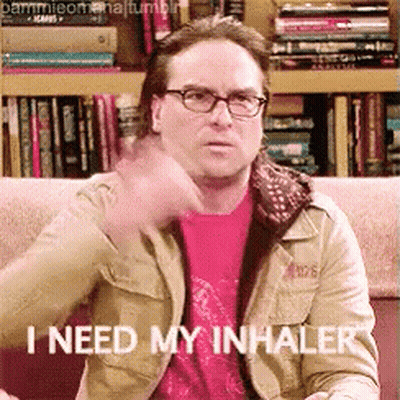 A Man Wearing Glasses Is Sitting On A Couch And Says " I Need My Inhaler " GIF