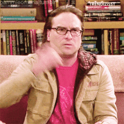 A Man Wearing Glasses Is Sitting On A Couch In Front Of A Bookshelf That Says Trendizisst On It GIF