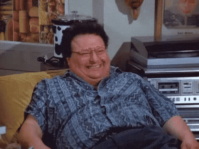 A Man Wearing Glasses Is Sitting On A Couch Laughing . GIF