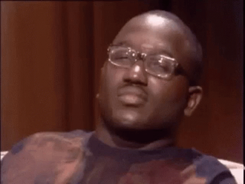 A Man Wearing Glasses Is Sitting On A Couch Making A Funny Face And Saying Wack . GIF