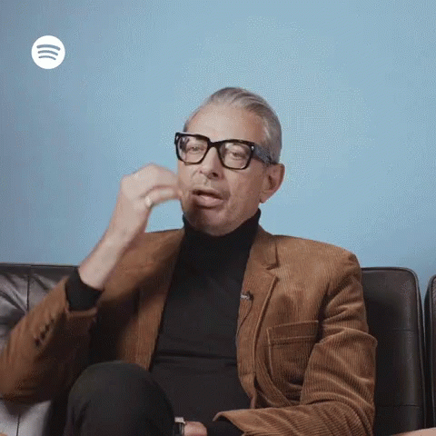 A Man Wearing Glasses Is Sitting On A Couch With A Spotify Logo In The Background GIF