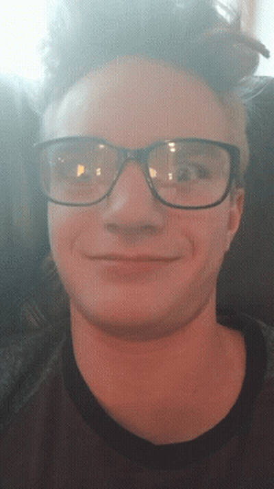 A Man Wearing Glasses Is Smiling And Looking Down GIF