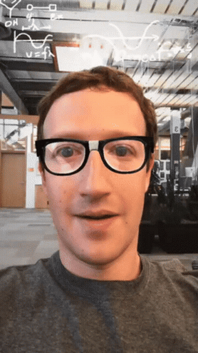 A Man Wearing Glasses Is Smiling In Front Of A Sign That Says " E " On It GIF