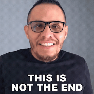 A Man Wearing Glasses Is Smiling In Front Of A Sign That Says " This Is Not The End " GIF