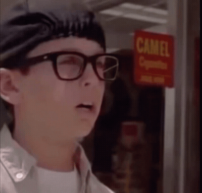 A Man Wearing Glasses Is Standing In Front Of A Camel Cigarette Sign GIF