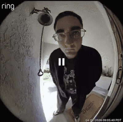 A Man Wearing Glasses Is Standing In Front Of A Door With A Ring Camera . GIF