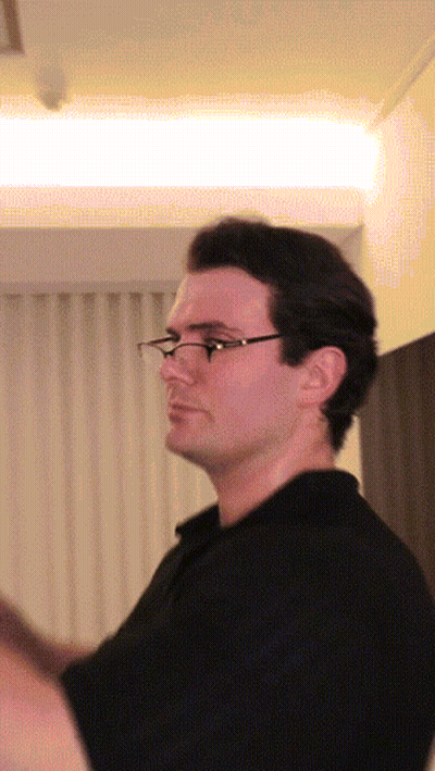 A Man Wearing Glasses Is Standing In Front Of A White Curtain GIF