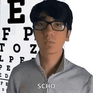A Man Wearing Glasses Is Standing In Front Of An Eye Chart And Making A Funny Face . GIF
