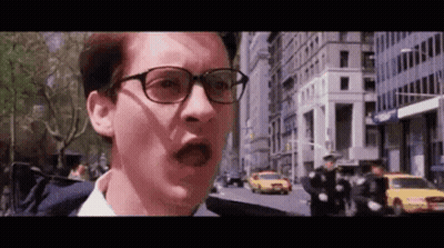 A Man Wearing Glasses Is Standing On A City Street With A Shocked Look On His Face . GIF