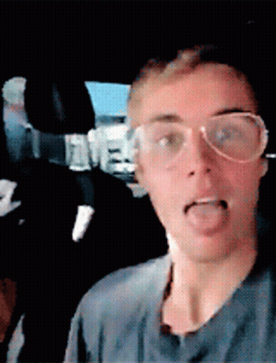 A Man Wearing Glasses Is Sticking His Tongue Out In A Car GIF