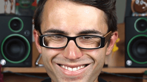 A Man Wearing Glasses Makes A Funny Face In Front Of Green Speakers GIF