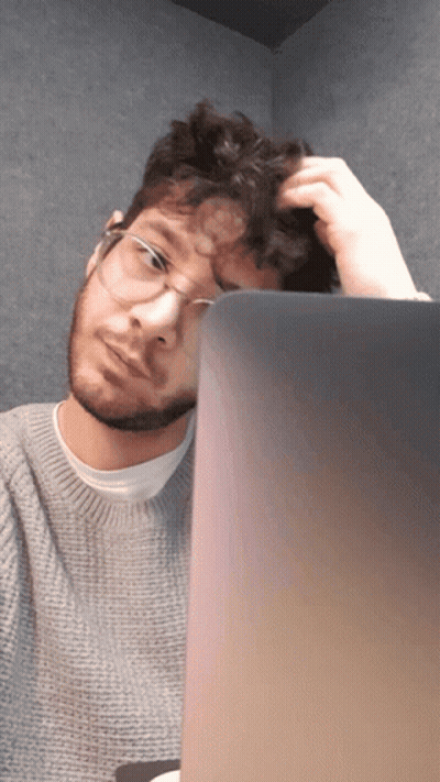 A Man Wearing Glasses Scratches His Head While Looking At A Laptop Screen GIF