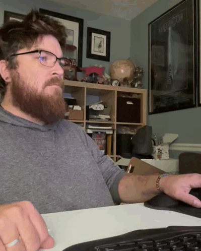 A Man Wearing Glasses Sits At A Desk In Front Of A Poster For Star Wars The Force Awakens GIF