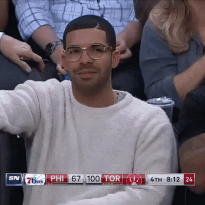 A Man Wearing Glasses Sits In A Stadium Watching A Basketball Game Between The 76Ers And The Tor GIF