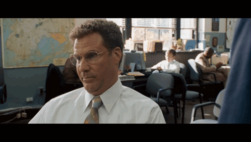 A Man Wearing Glasses Sits In An Office With A Map Behind Him GIF