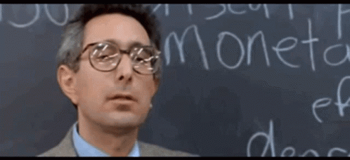 A Man Wearing Glasses Stands In Front Of A Blackboard That Says Moneta GIF