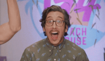 A Man Wearing Glasses Stands In Front Of A Peach House Sign GIF