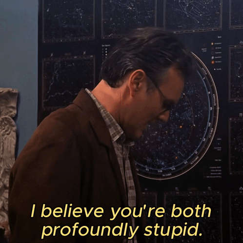 A Man Wearing Glasses Stands In Front Of A Poster That Says I Believe You 'Re Both Profoundly Stupid GIF