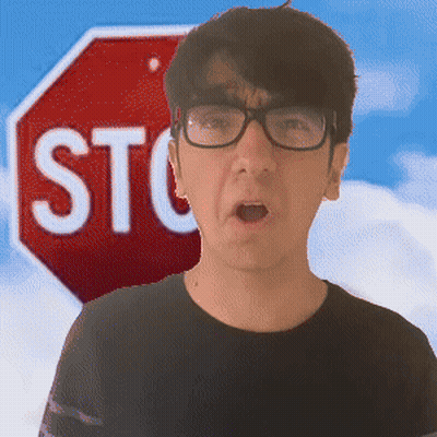 A Man Wearing Glasses Stands In Front Of A Red Stop Sign GIF