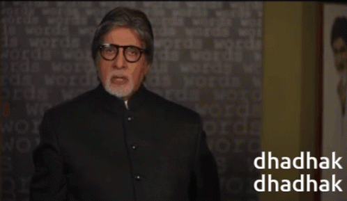 A Man Wearing Glasses Stands In Front Of A Wall With Words On It And The Words Dhadhak Dhadhak On The Bottom GIF