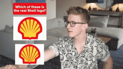 A Man Wearing Glasses Stands In Front Of Two Shell Logos GIF