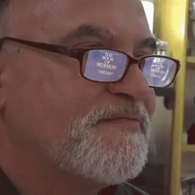 A Man Wearing Glasses With The Book Of Mormon Reflected In The Lenses GIF
