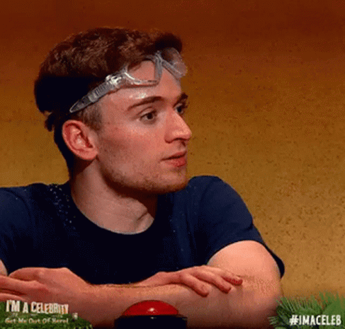 A Man Wearing Goggles And A Blue Shirt Is Sitting At A Table With His Arms Crossed . GIF