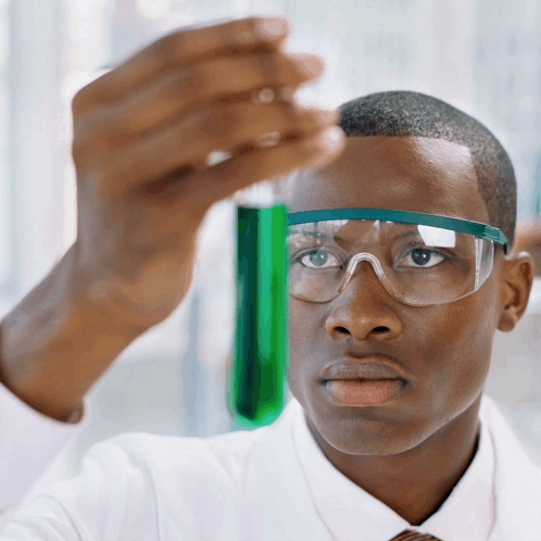 A Man Wearing Goggles Looks At A Green Liquid In A Beaker GIF
