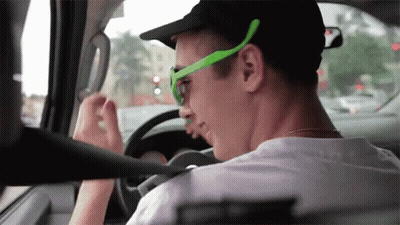 A Man Wearing Green Sunglasses And A Black Hat Driving A Car GIF