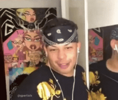 A Man Wearing Headphones And A Bandana Is Looking At Himself In The Mirror . GIF