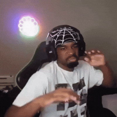 A Man Wearing Headphones And A Bandana With A Spider Web On It Is Sitting In A Chair . GIF
