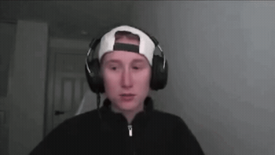A Man Wearing Headphones And A Baseball Cap Is Looking At The Camera . GIF
