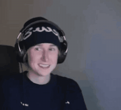 A Man Wearing Headphones And A Beanie Is Smiling While Sitting In Front Of A Computer . GIF