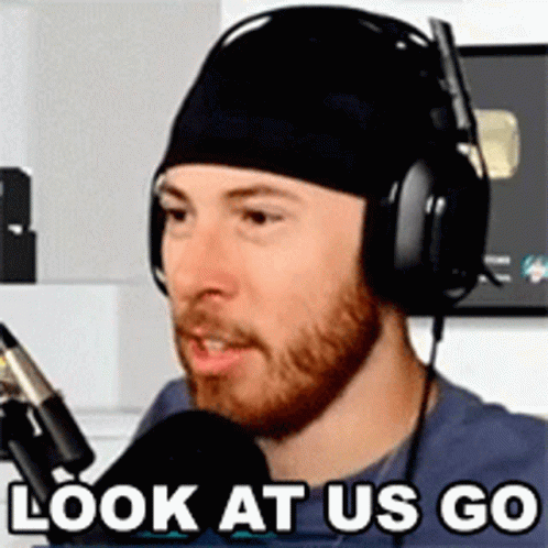 A Man Wearing Headphones And A Beanie Is Talking Into A Microphone And Says `` Look At Us Go '' . GIF