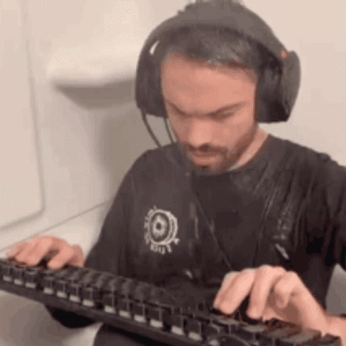 A Man Wearing Headphones And A Black Shirt Is Typing On A Keyboard . GIF