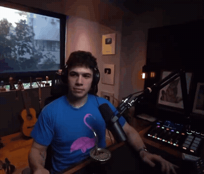 A Man Wearing Headphones And A Blue Flamingo Shirt Is Sitting At A Desk In Front Of A Microphone GIF
