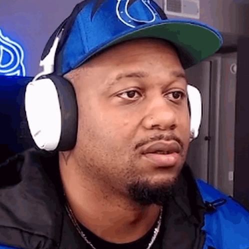 A Man Wearing Headphones And A Blue Hat Is Making A Funny Face . GIF