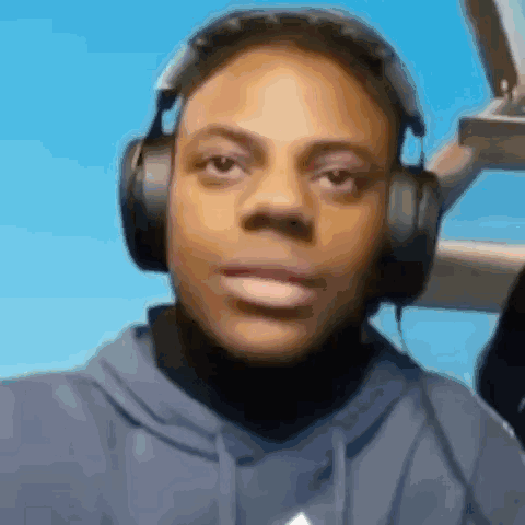 A Man Wearing Headphones And A Blue Hoodie Is Looking At The Camera . GIF