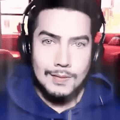 A Man Wearing Headphones And A Blue Hoodie Is Smiling . GIF