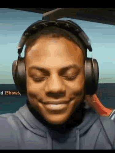 A Man Wearing Headphones And A Blue Hoodie Is Smiling . GIF