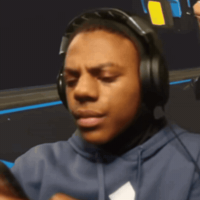A Man Wearing Headphones And A Blue Hoodie Looks At His Phone GIF