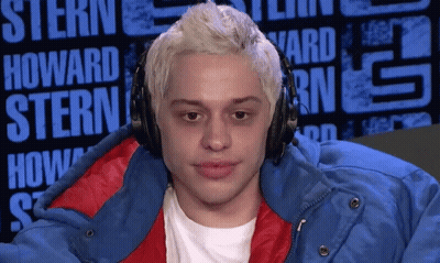 A Man Wearing Headphones And A Blue Jacket Is Sitting In Front Of A Sign That Says Howard Stern GIF
