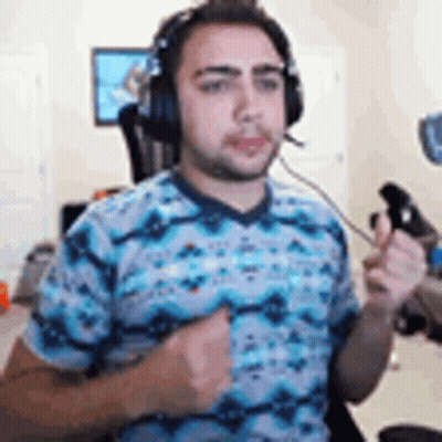 A Man Wearing Headphones And A Blue Shirt Is Holding A Controller In His Hand . GIF